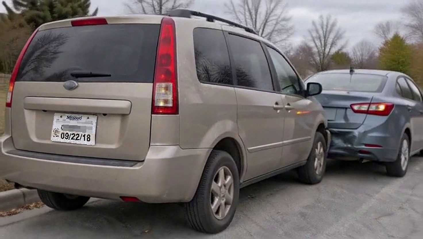 A minivan with a paper tag after a rear-end collision with a sedan, parked on a residential street.